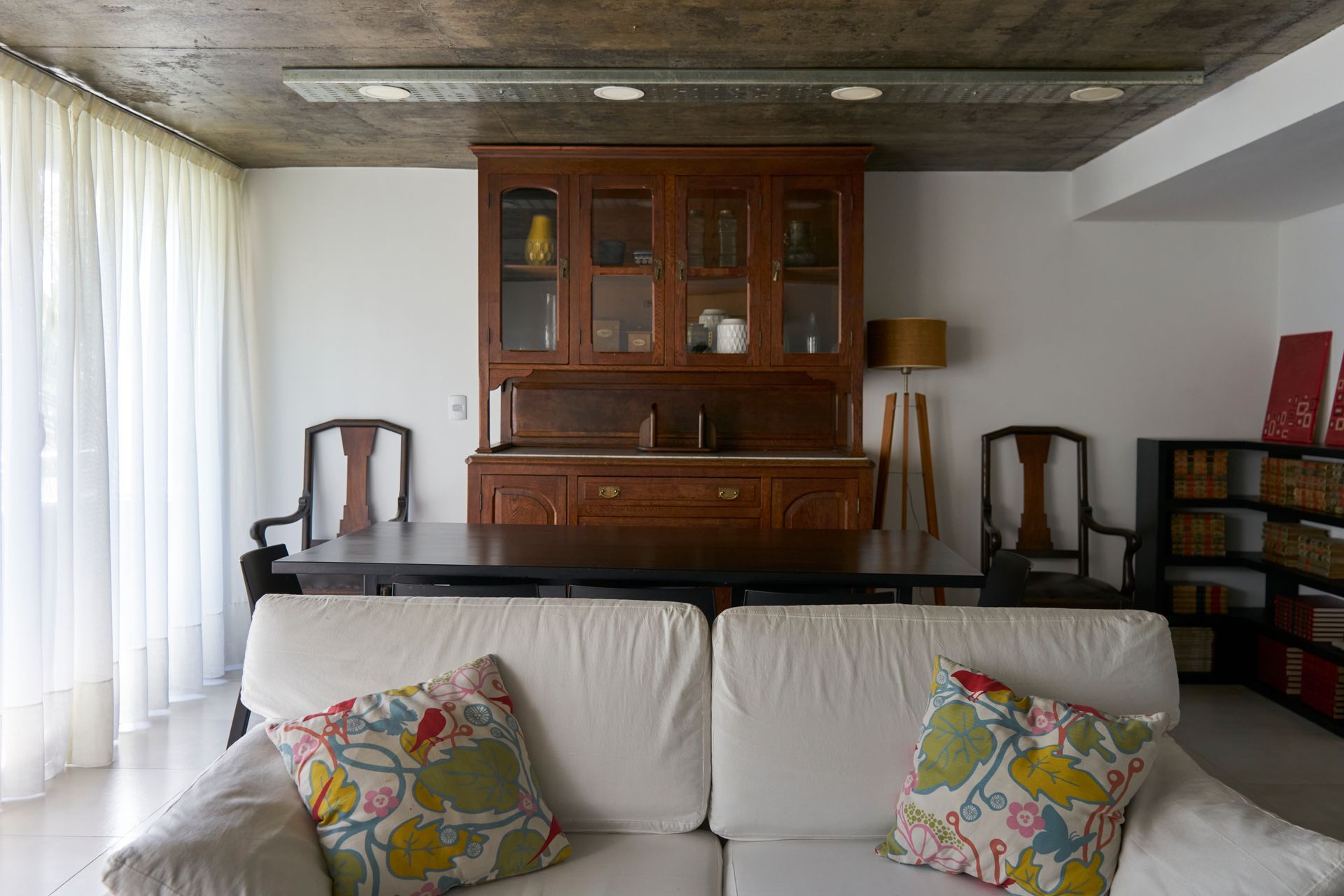 Sala de estar con sofá blanco, mesa de madera oscura, aparador, sillas y estanterías.