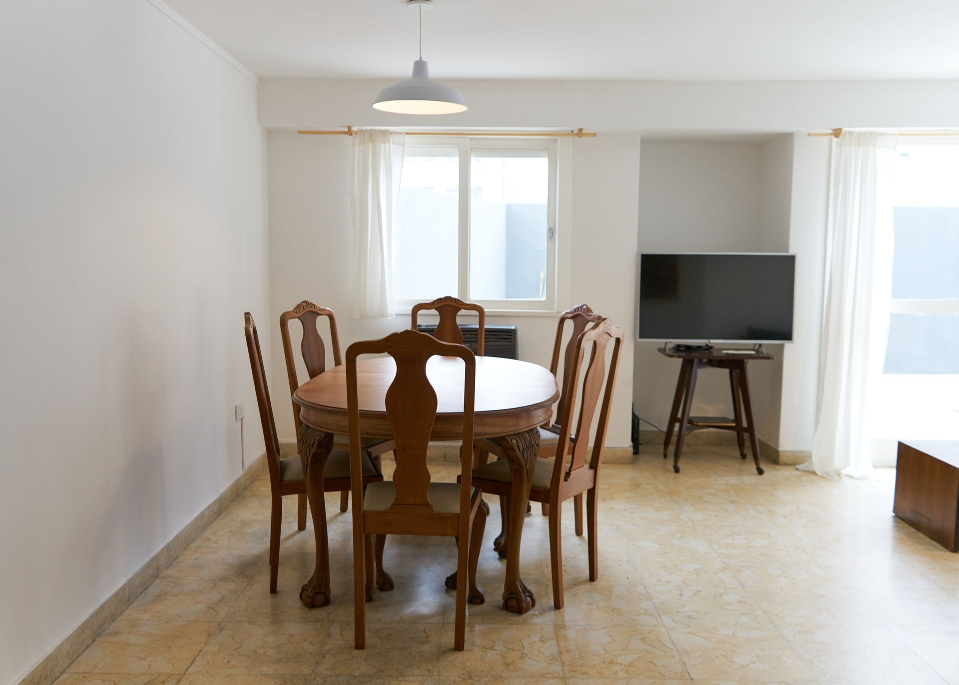 Comedor con mesa y sillas de madera, ventana con cortinas transparentes y TV.