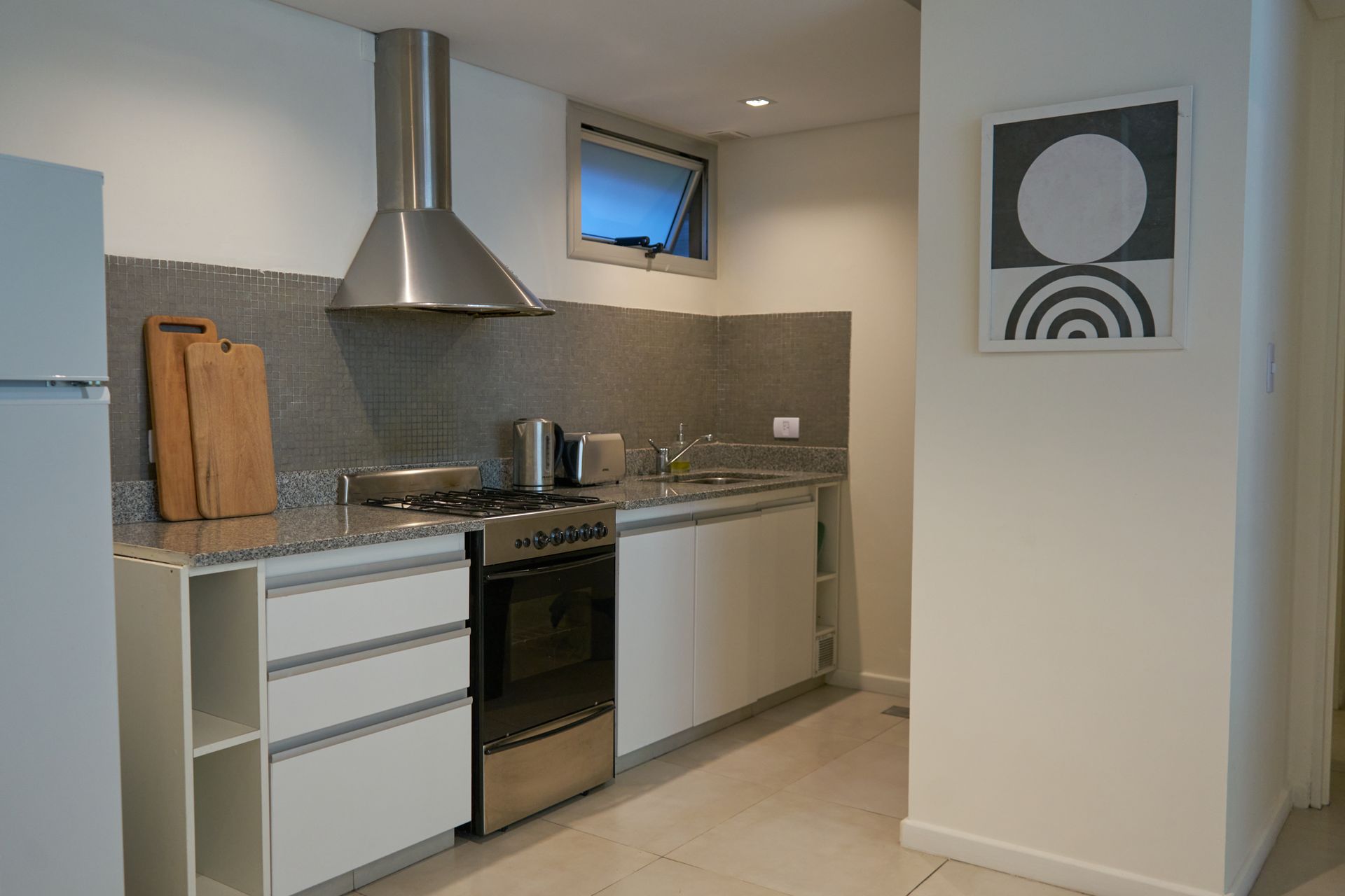 Cocina moderna con gabinetes blancos, electrodomésticos de acero inoxidable y protector contra salpicaduras gris.