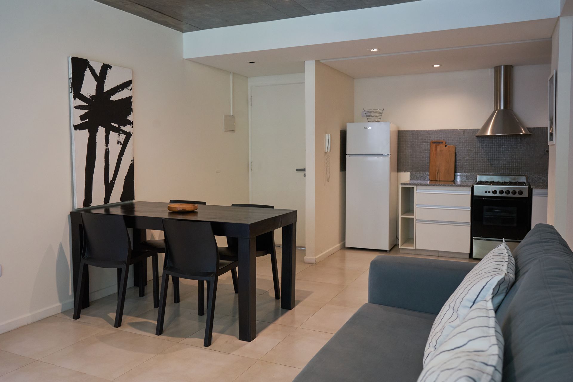 Interior de apartamento moderno con mesa de comedor, sillas, cocina y sofá.