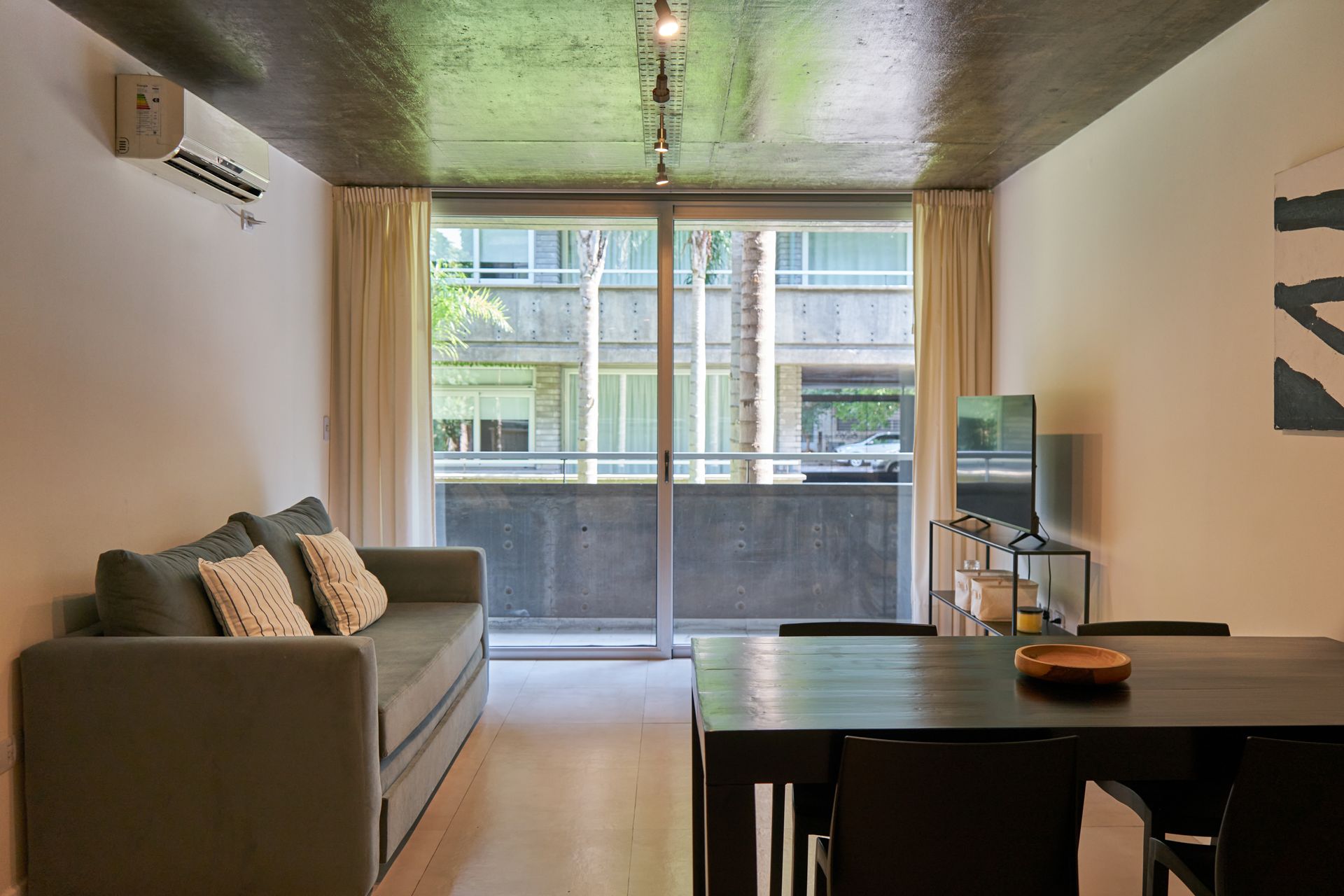 Sala de estar con sofá, mesa de comedor, balcón y vista al exterior.