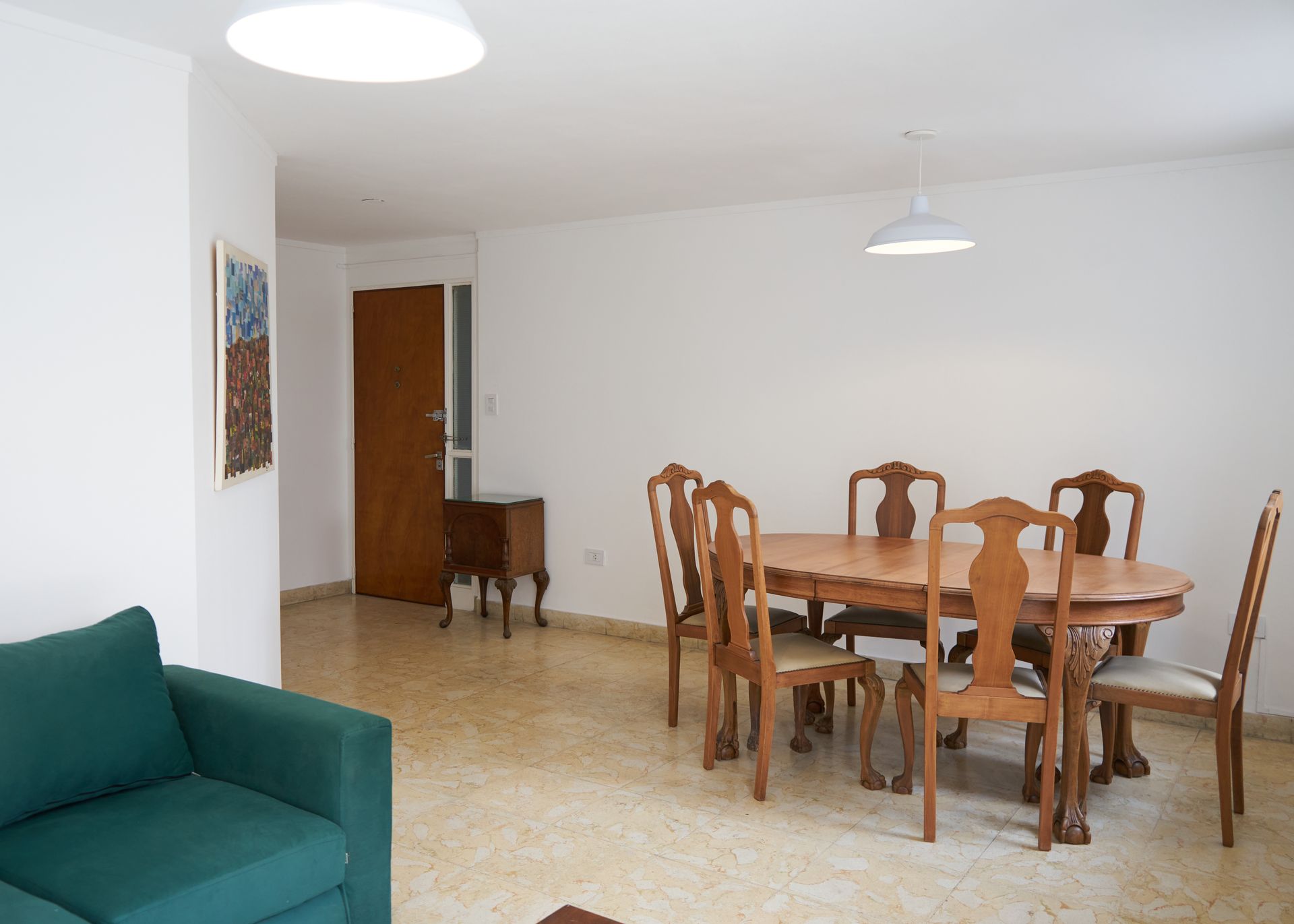 Una sala de estar con un sofá verde, un juego de comedor de madera y puerta de entrada a otras habitaciones.