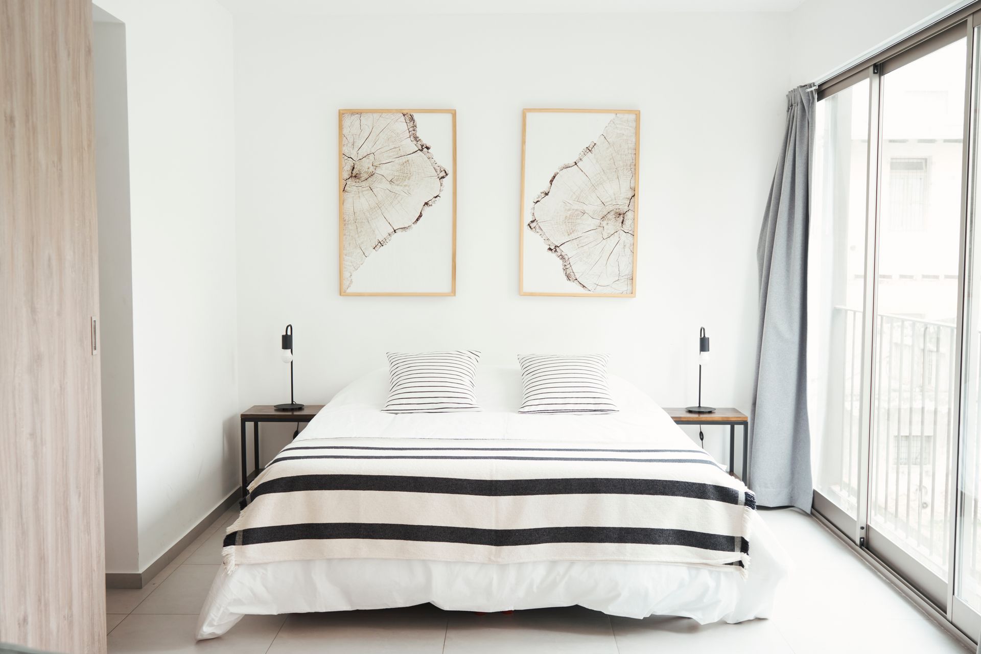 Dormitorio con cama blanca, dos mesitas de noche, arte y puertas corredizas de vidrio.