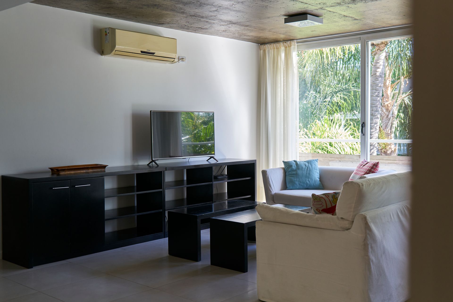 Sala de estar con TV, sofá y gran ventanal con vista a la vegetación.