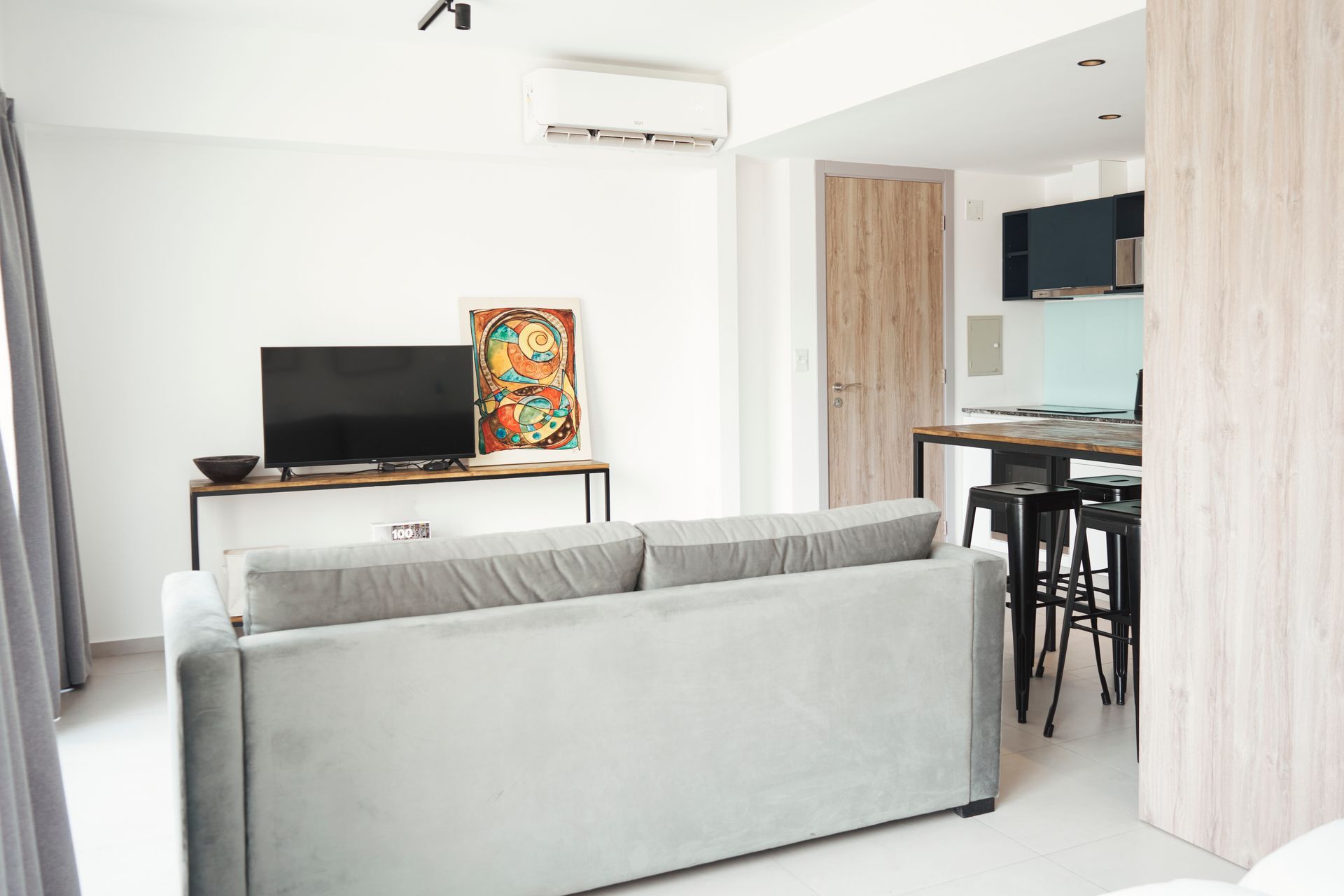 Sala de estar con sofá gris, TV en consola y cocina abierta con barra de desayuno.