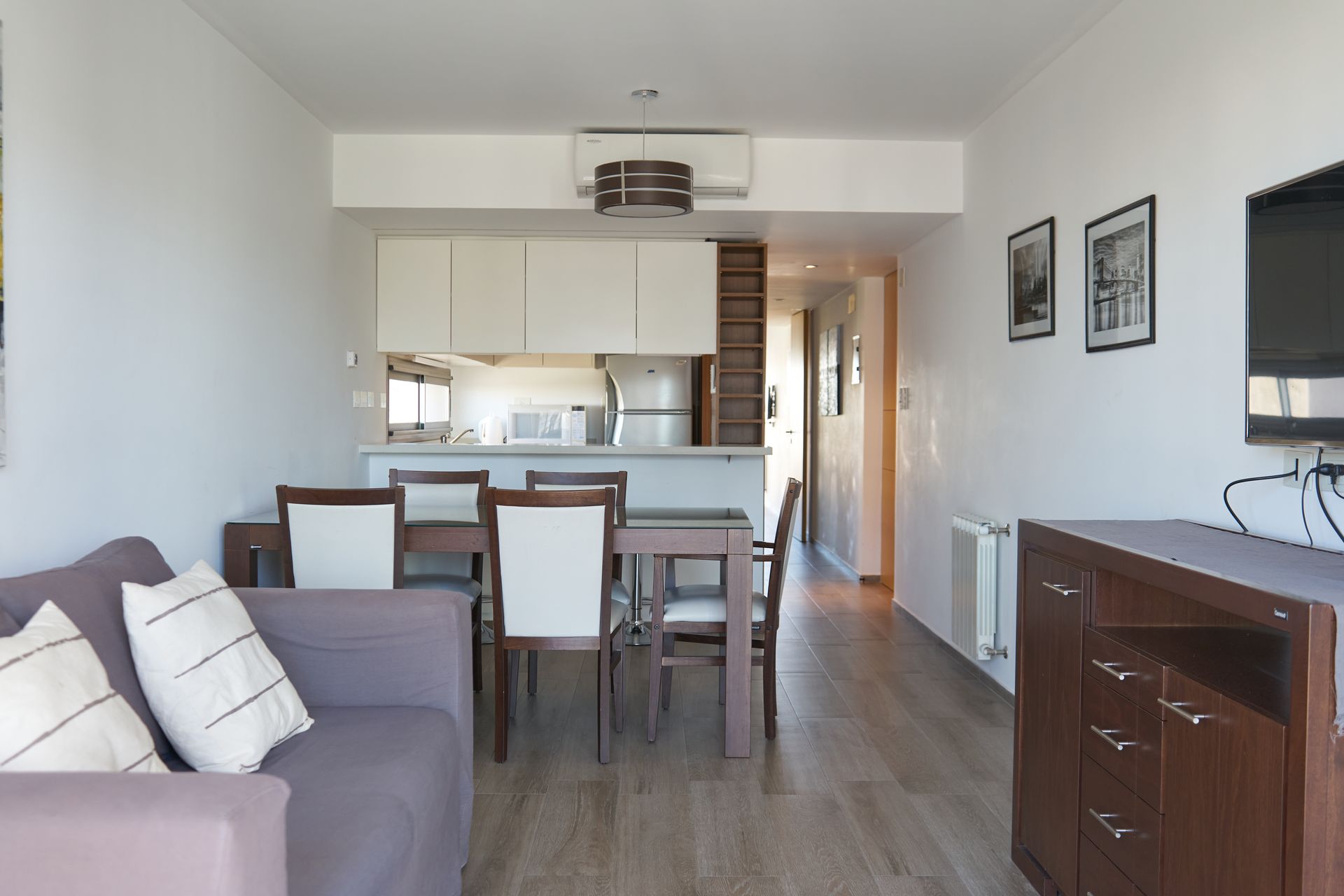 Sala de estar y comedor: sofá morado, mesa de comedor con sillas, cocina abierta y TV.