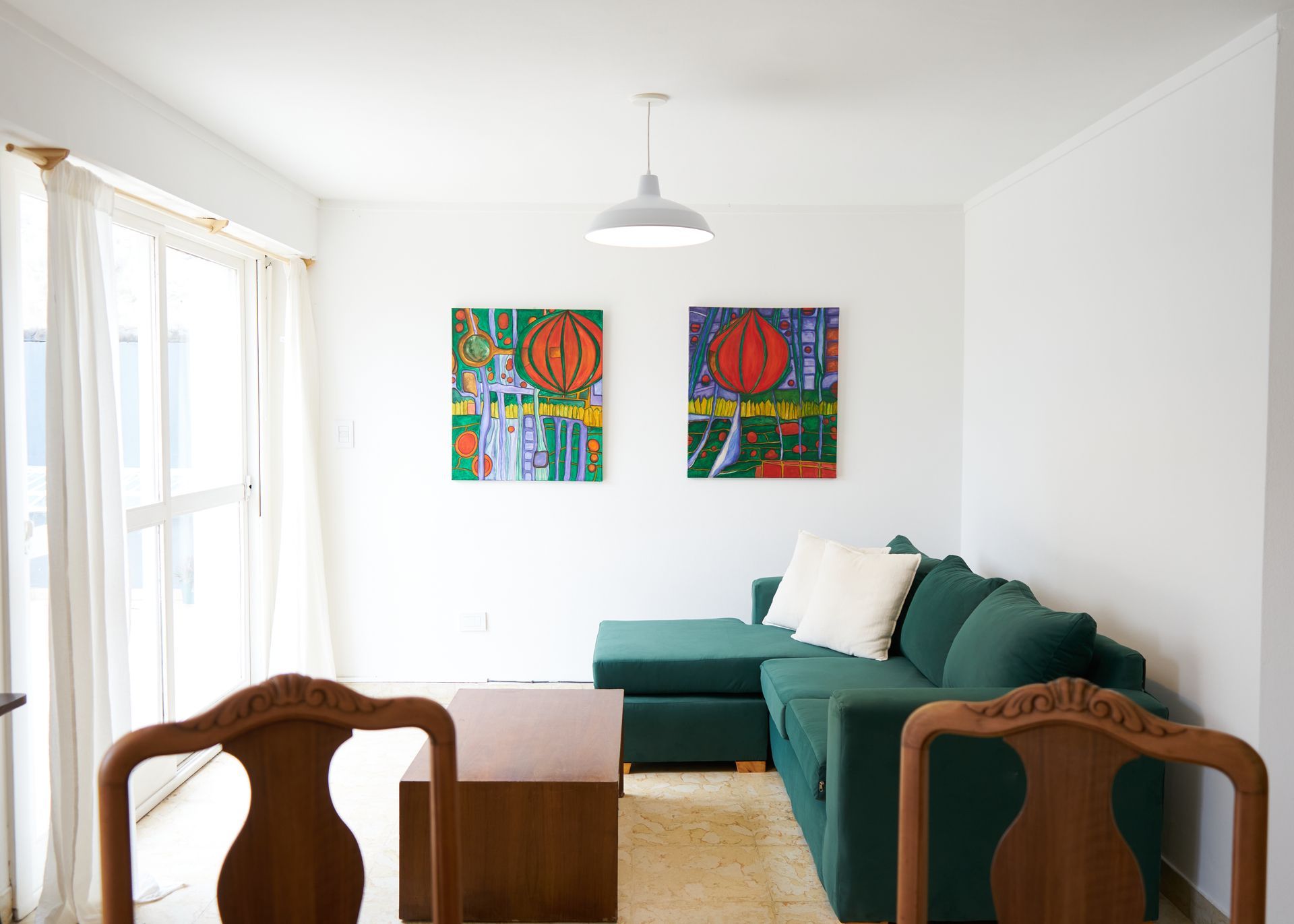 Sala de estar con sofá seccional verde, dos cuadros abstractos y sillas de madera.