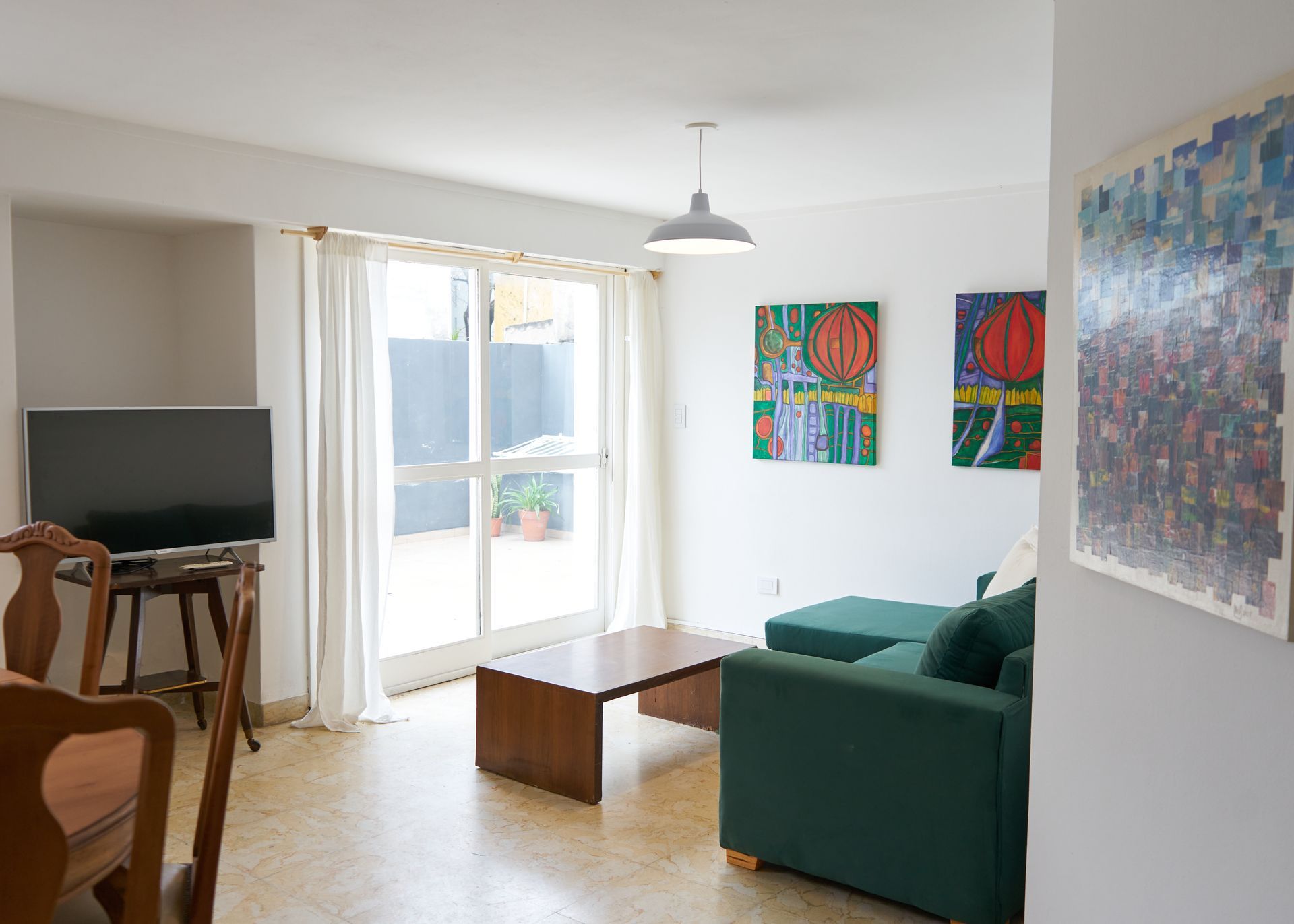 Sala de estar con sofá verde, arte, TV y puerta corrediza de vidrio al patio.