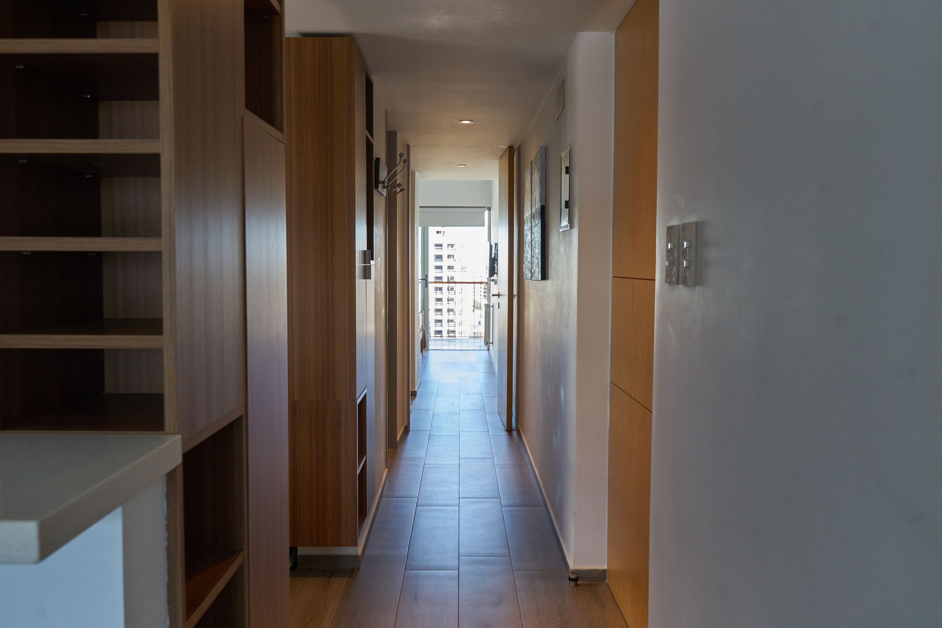 Pasillo con muebles de madera, estanterías y vista a un balcón al final.