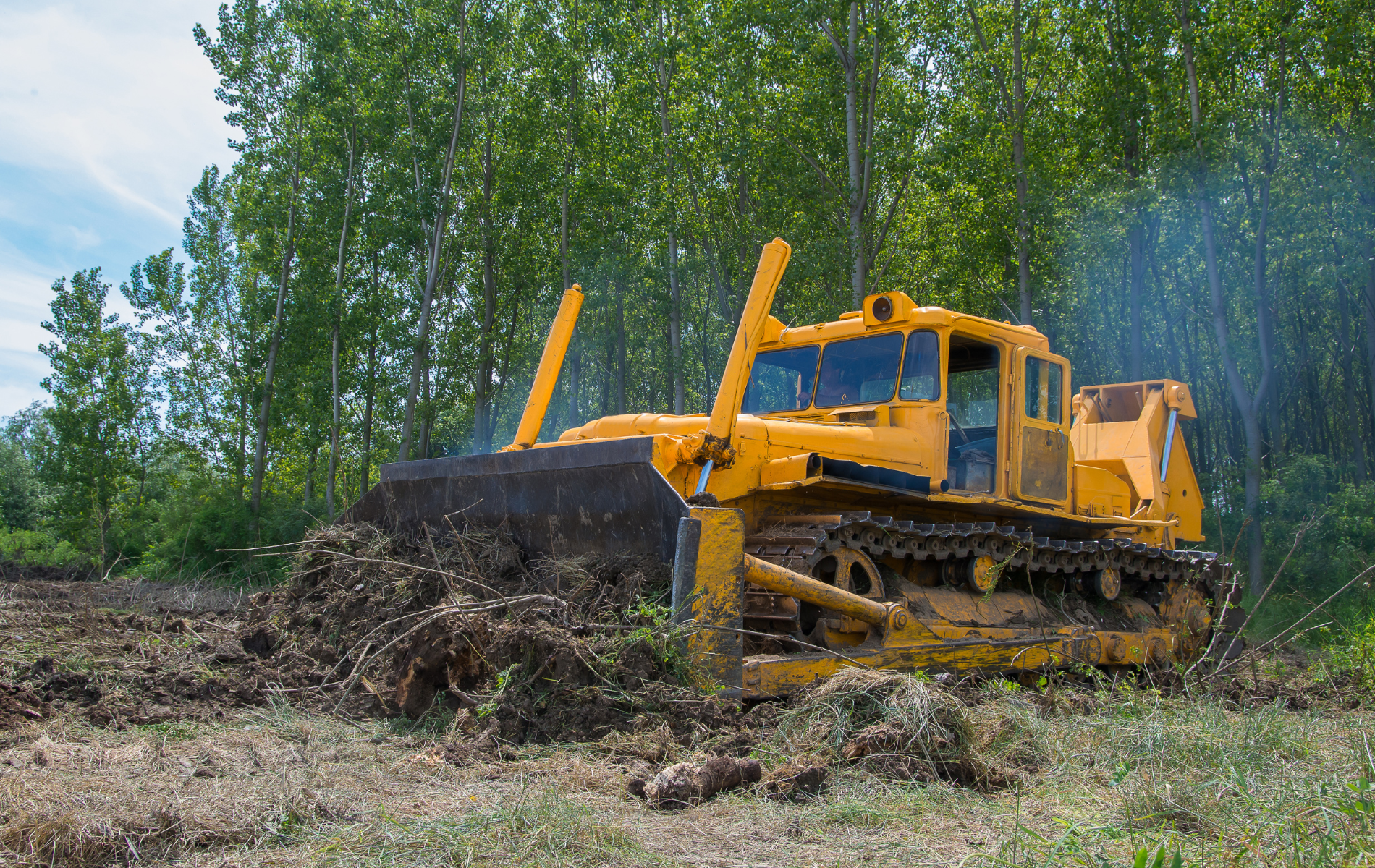 A yellow bulldozer is driving through a dirt field.