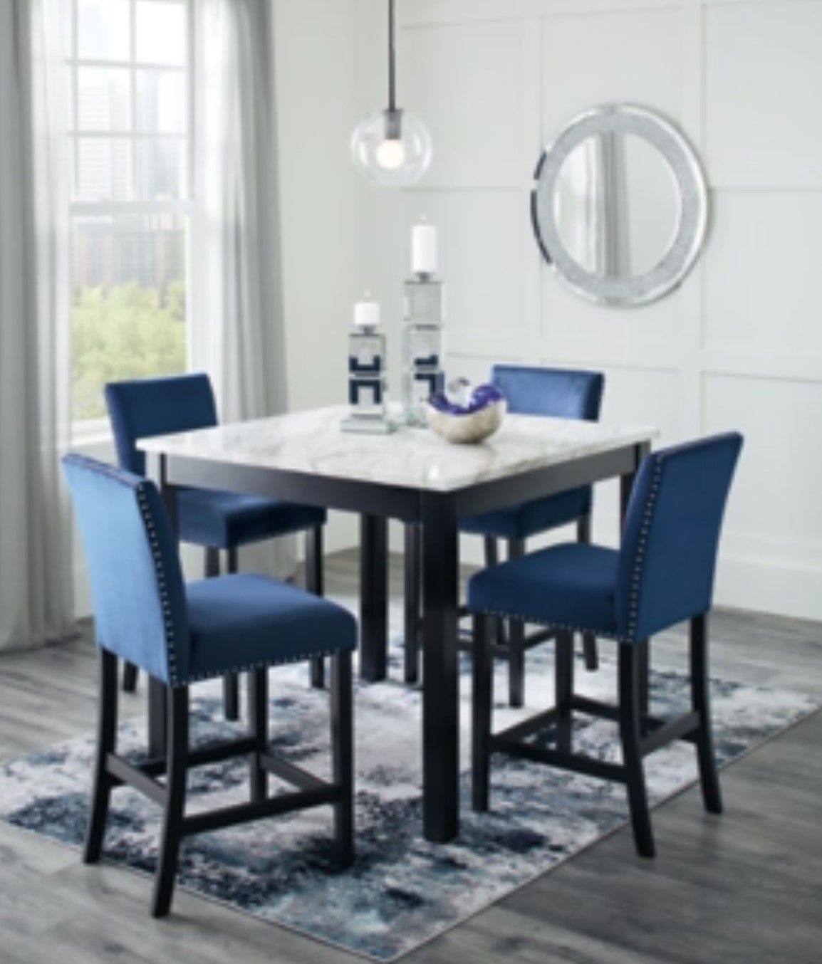 A square marble-topped dining table with four blue bar stools, set on a patterned rug.