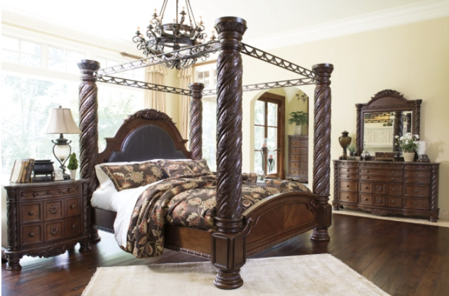 Elegant bedroom with a dark wood four-poster bed, dresser, and nightstand. Chandelier and window provide lighting.
