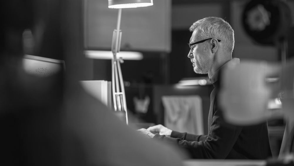 A man is sitting at a desk in front of a computer in a black and white photo.