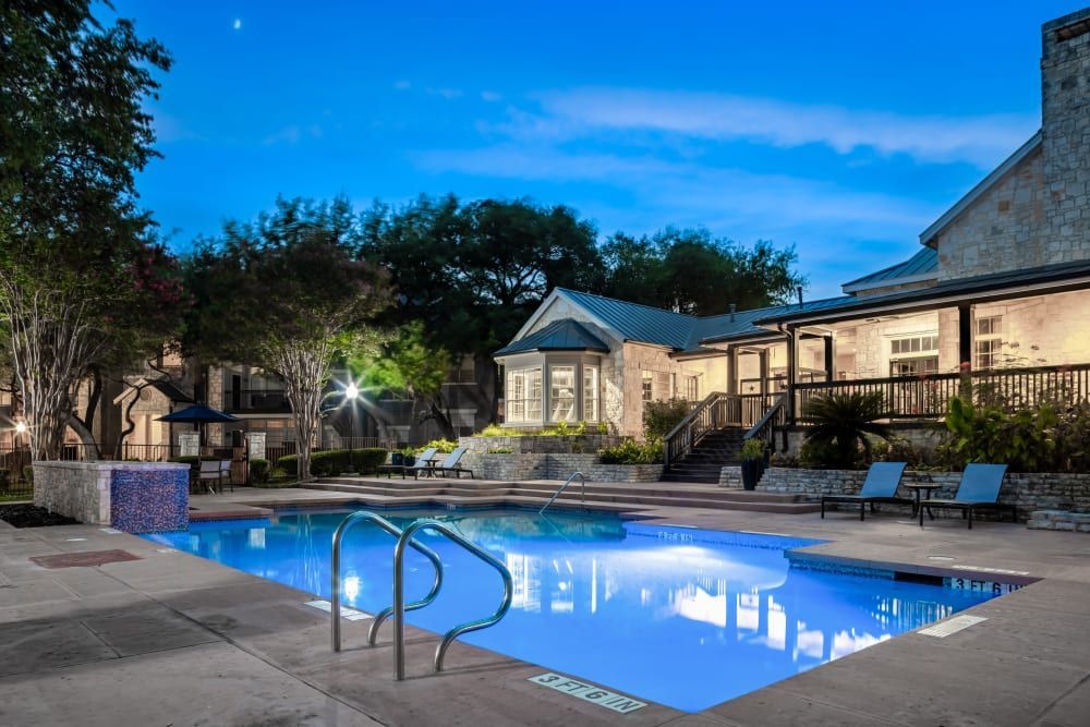 a large swimming pool is lit up at night in front of a building at Marquis at Deerfield in San Antonio, TX.
