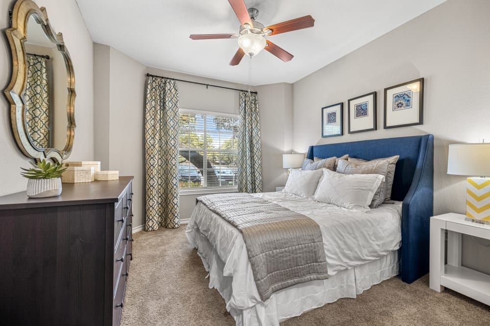 a bedroom with a bed, dresser, mirror, and ceiling fan at Marquis at Deerfield in San Antonio, TX.