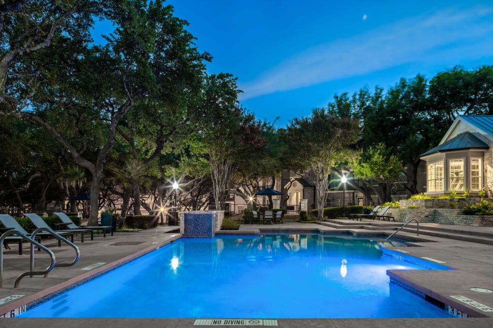a large swimming pool is lit up at night surrounded by trees and chairs at Marquis at Deerfield in San Antonio, TX.