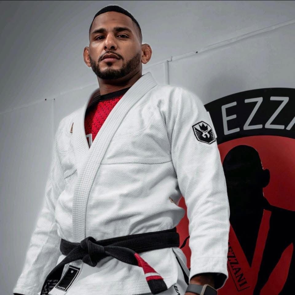Man in white Jiu-Jitsu uniform, black belt, standing in gym with 