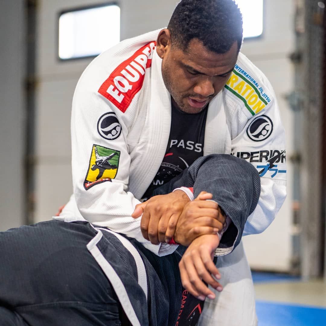 Man in a white gi, applying an armlock to a person on the ground during a Brazilian Jiu-Jitsu session.