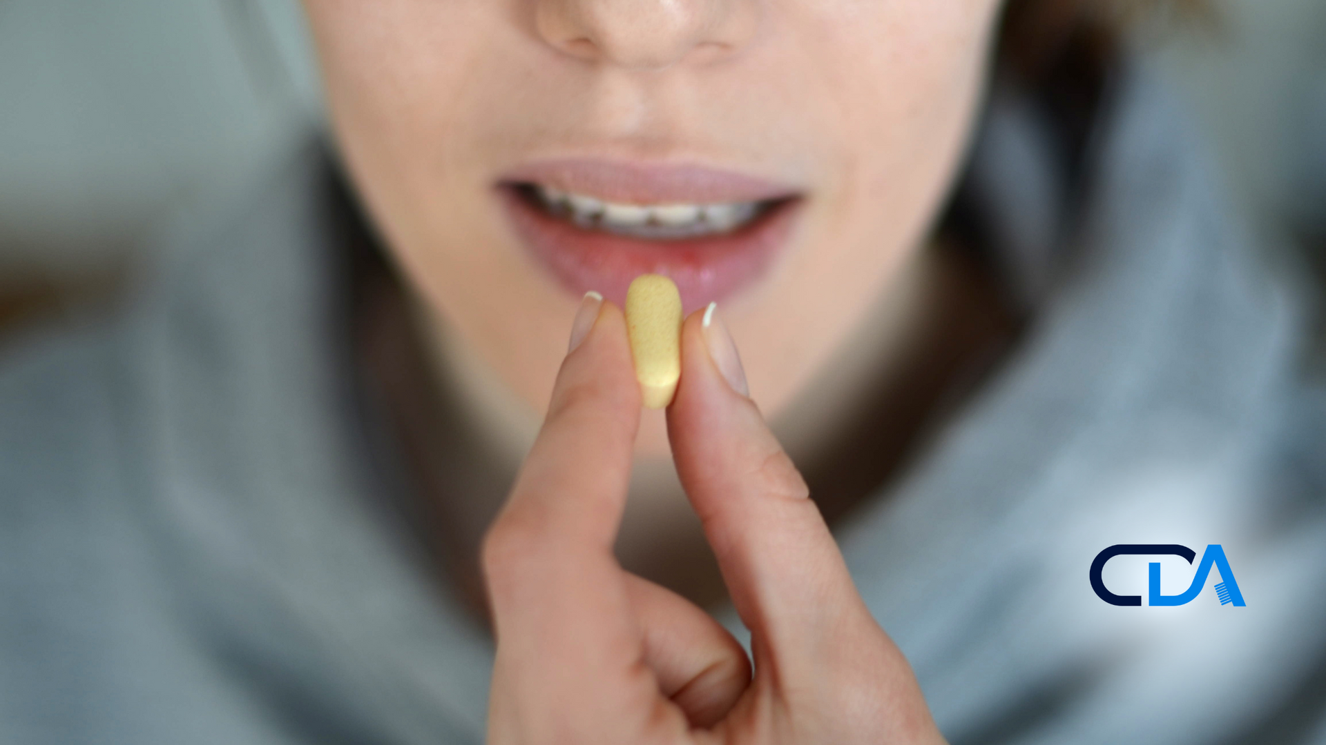 A woman is holding a pill in her hand in front of her mouth.