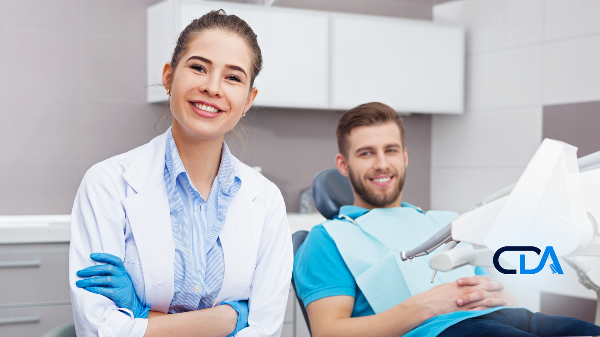 A female dentist is standing next to a man in a dental chair.