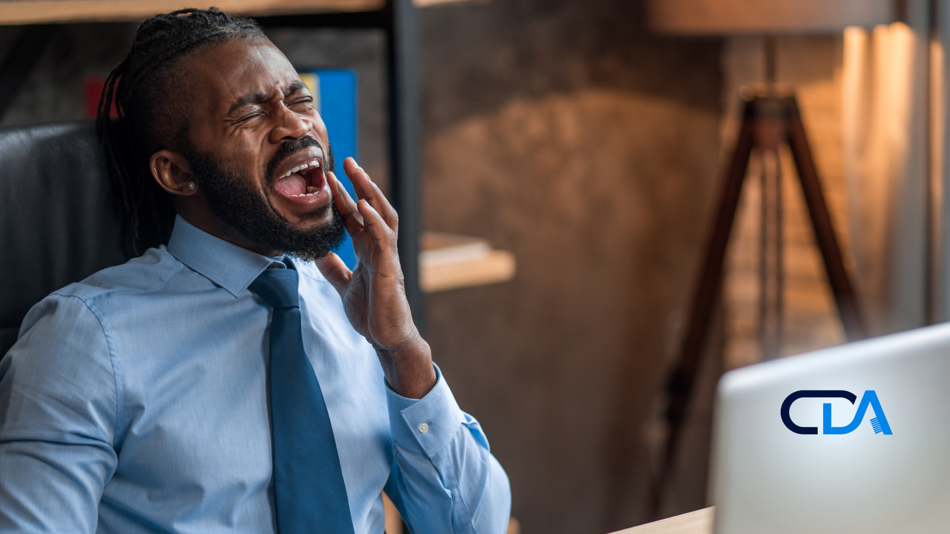 A man in a suit and tie is yawning in front of a laptop computer.