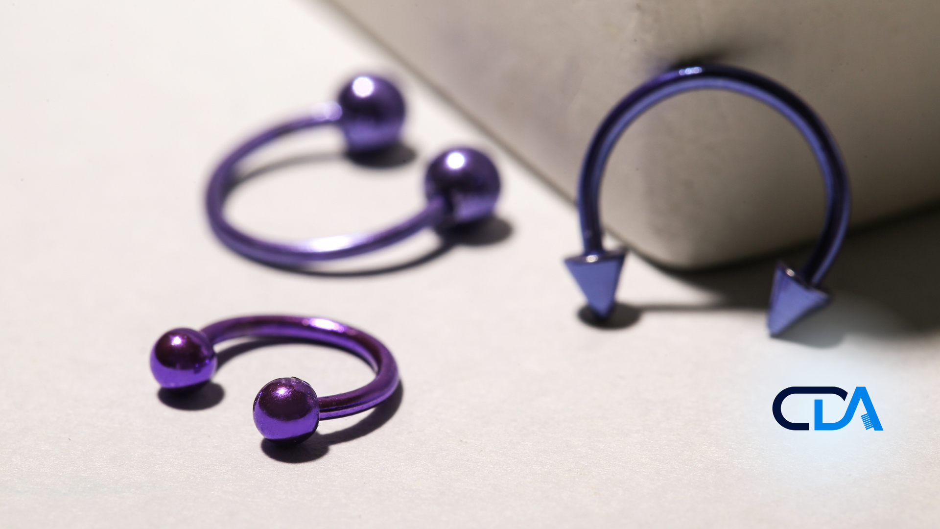 Three purple horseshoe piercings are on a white surface