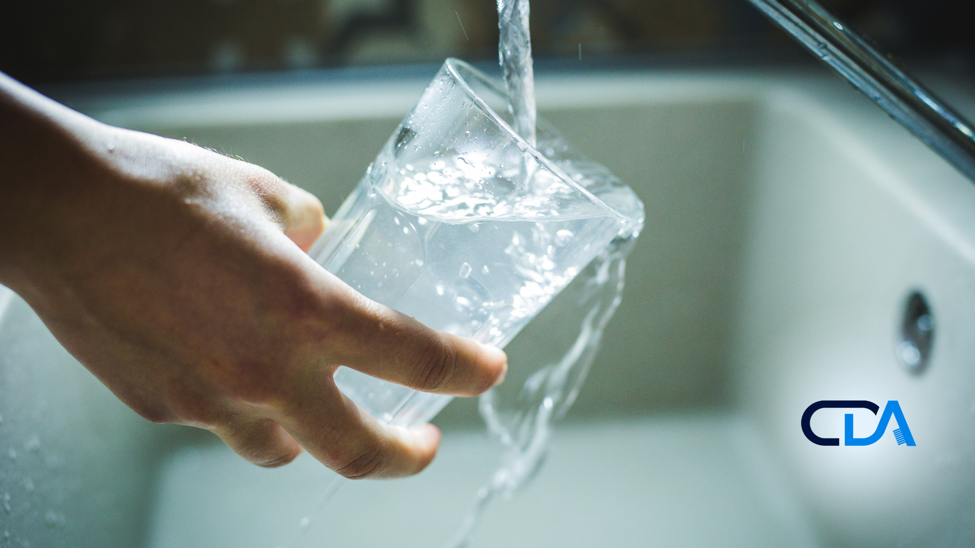 A person is pouring water into a glass in a sink.