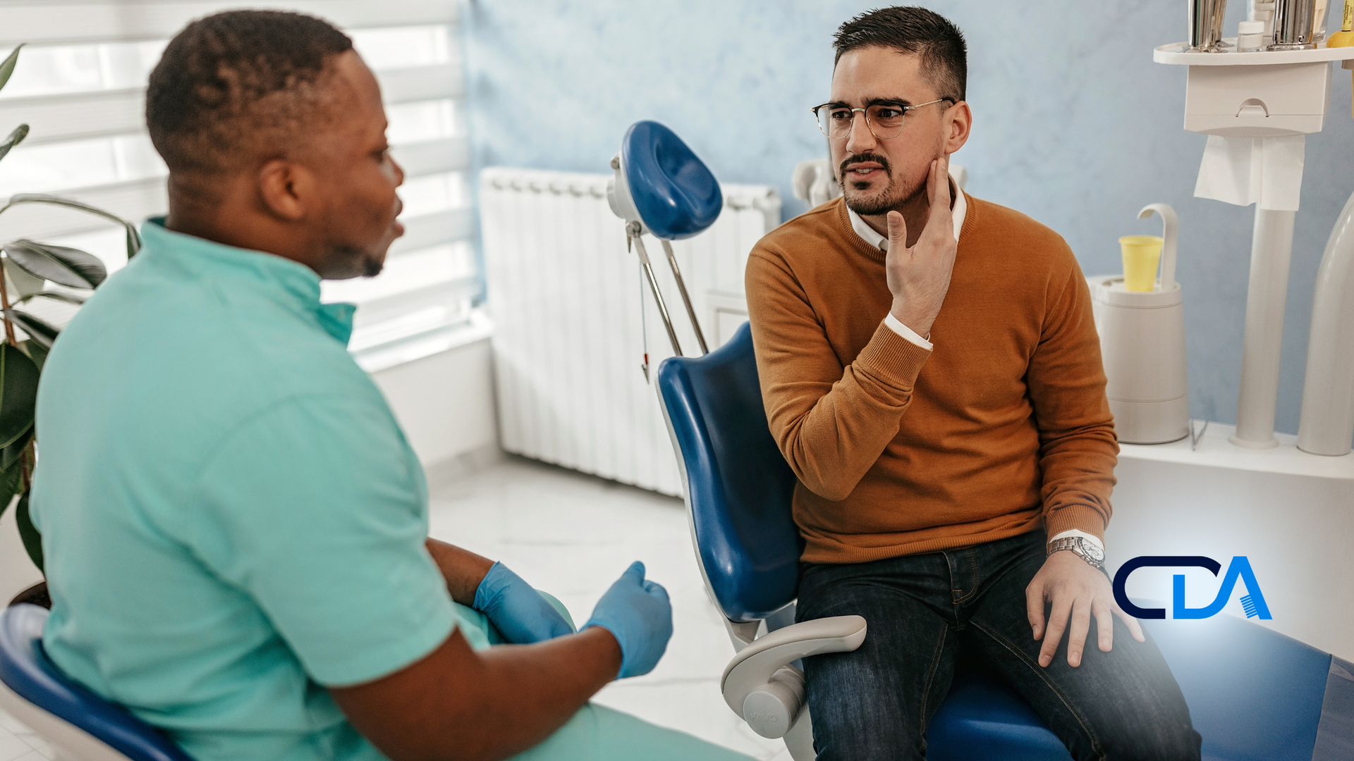 A man is sitting in a dental chair talking to a dentist.