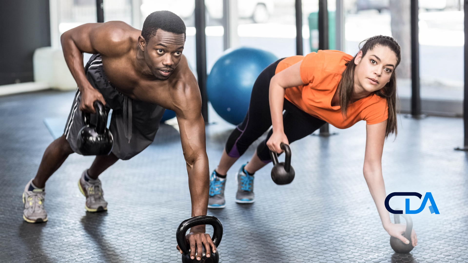 A man and a woman are doing push ups with kettlebells in a gym.