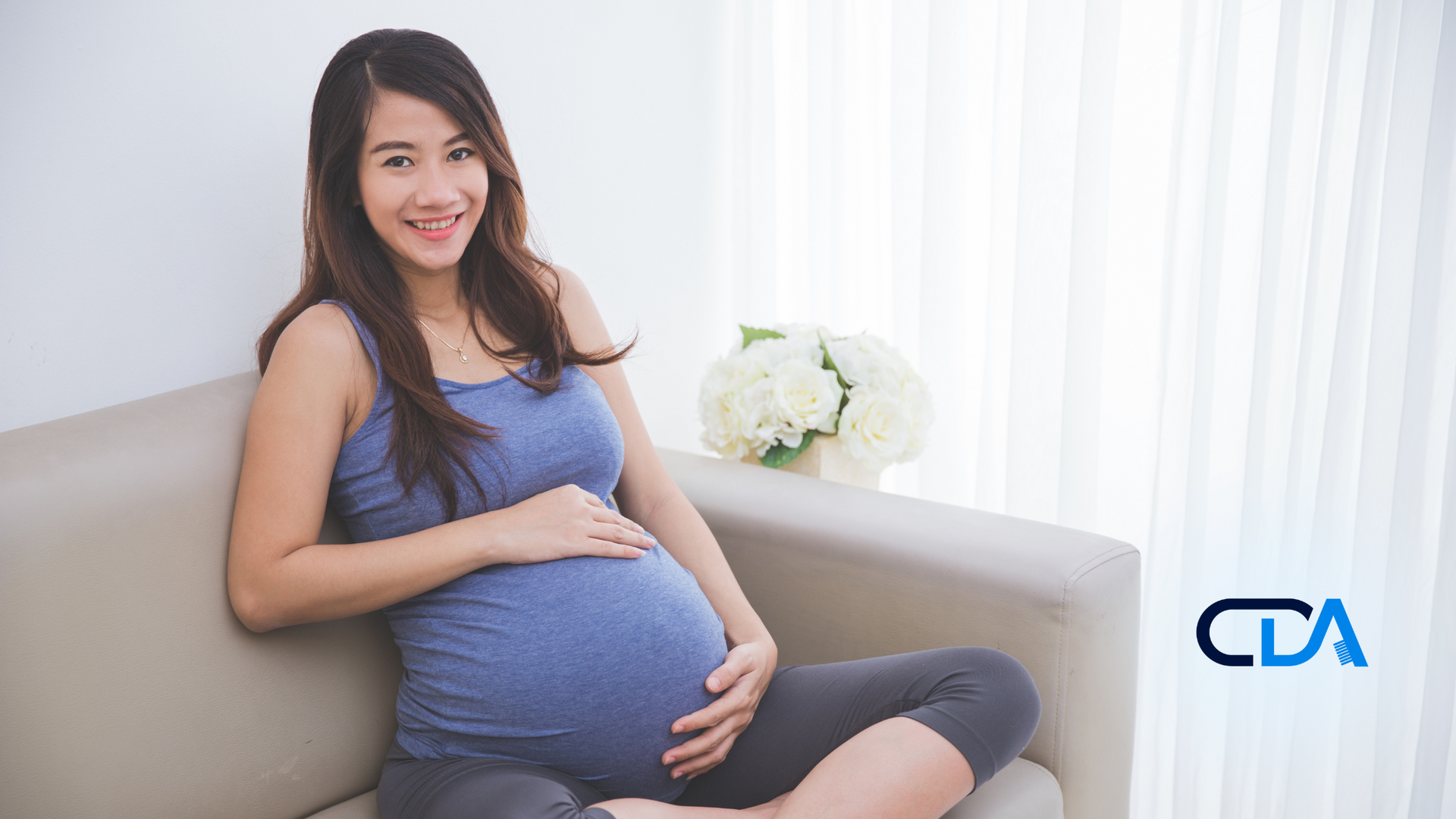 A pregnant woman is sitting on a couch holding her belly.