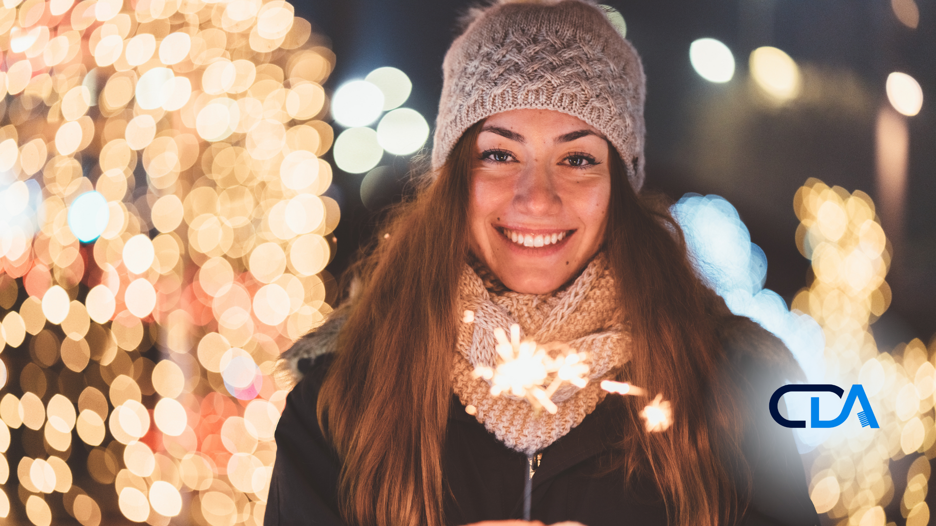 A woman is holding a sparkler in front of a christmas tree.