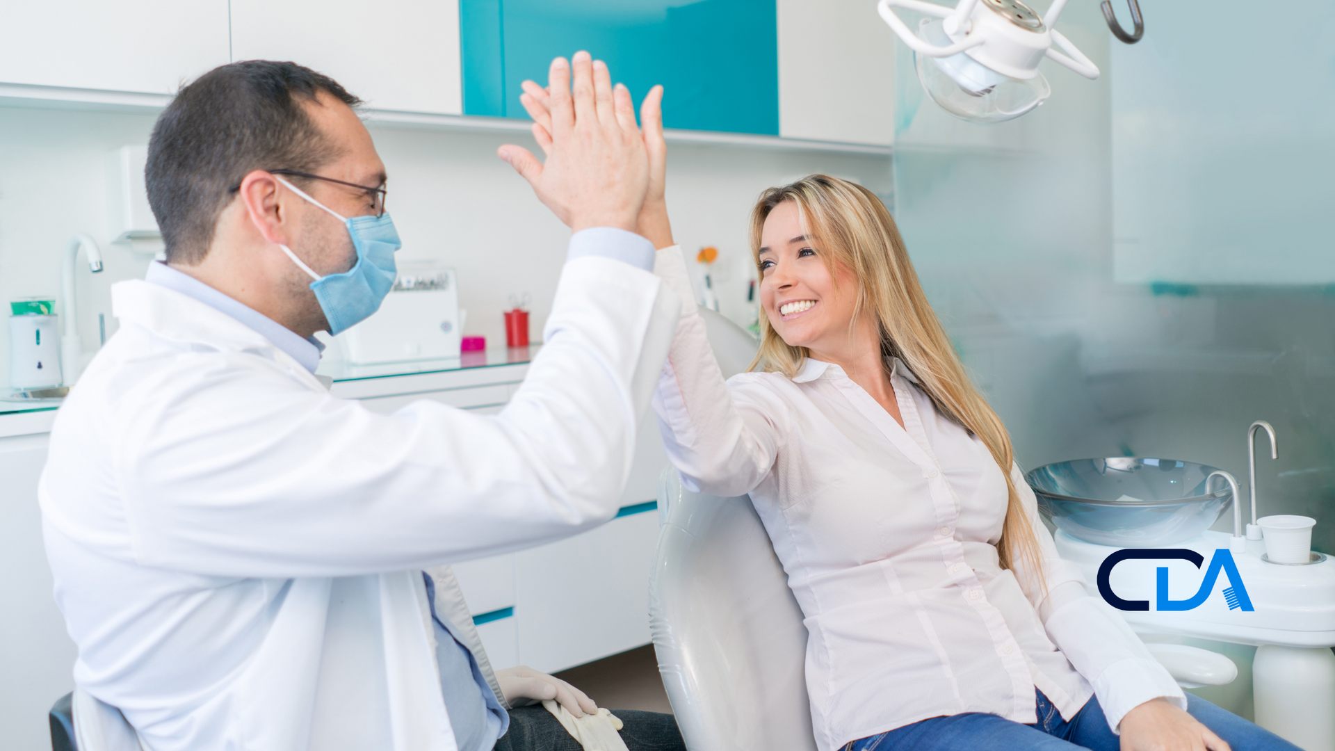 A dentist and a patient are giving each other a high five in a dental office.