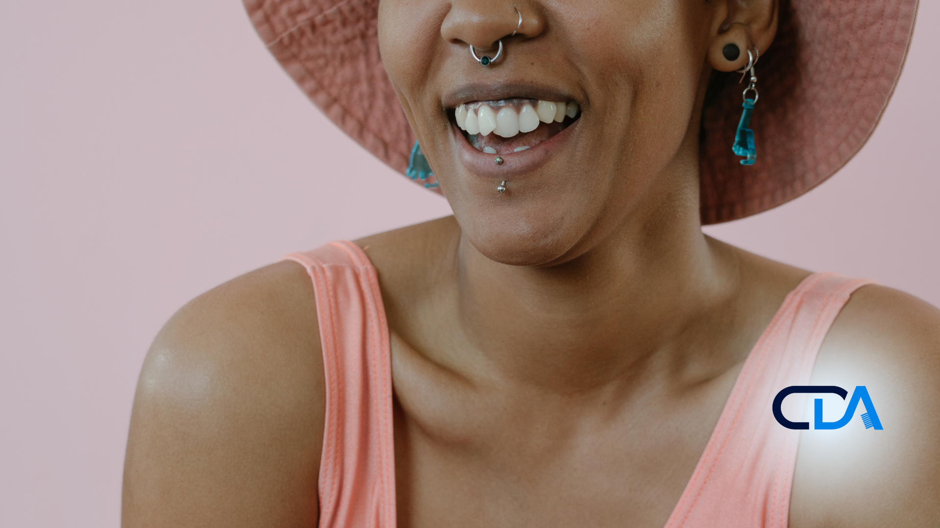 A woman wearing a hat and a pink tank top is smiling.