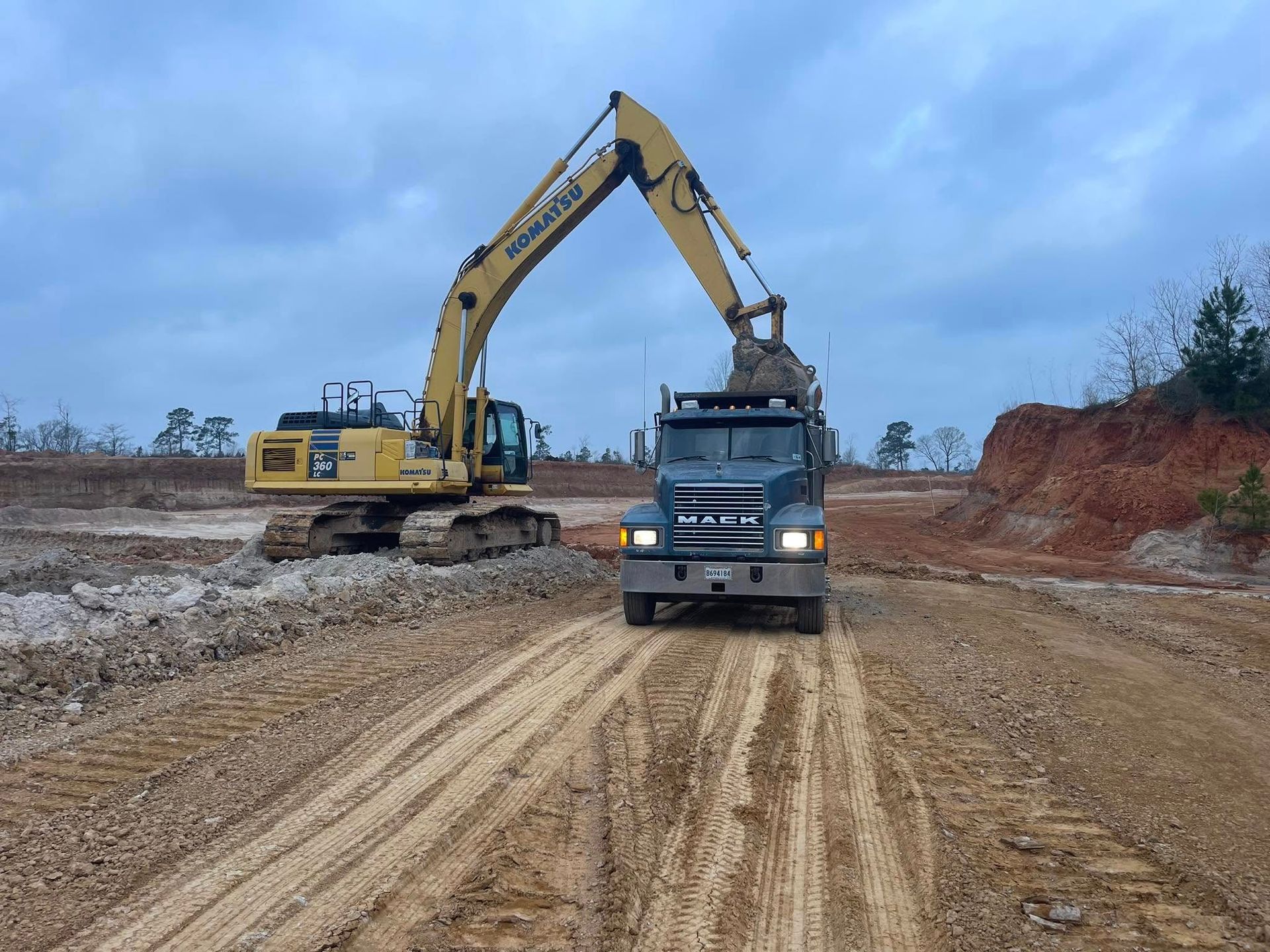 An excavator is loading dirt into a dump truck on a dirt road.