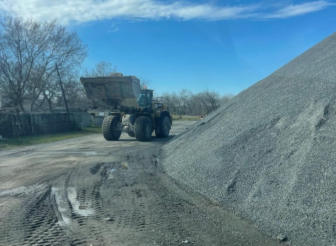 A bulldozer is driving down a dirt road next to a pile of gravel.