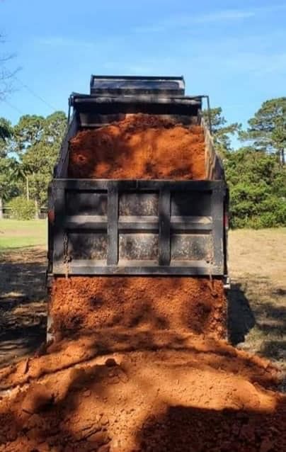 A dump truck is filled with dirt in a field.