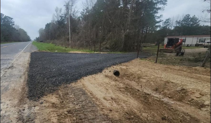 A tractor is driving down a dirt road next to a road.