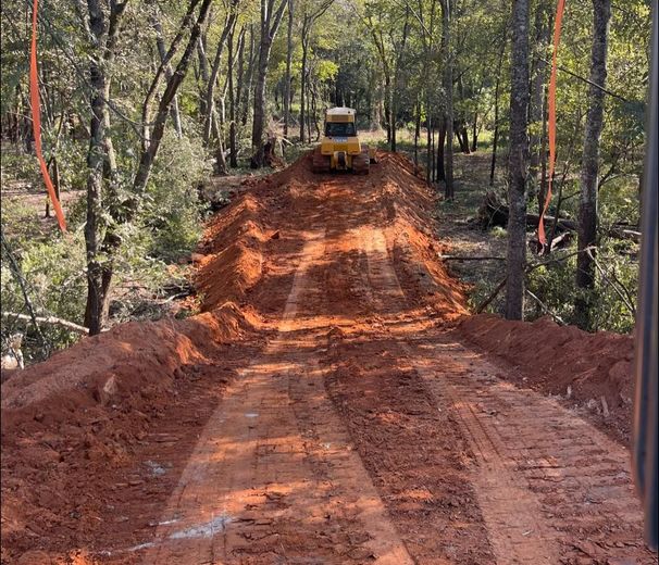 A bulldozer is driving down a dirt road in the woods.
