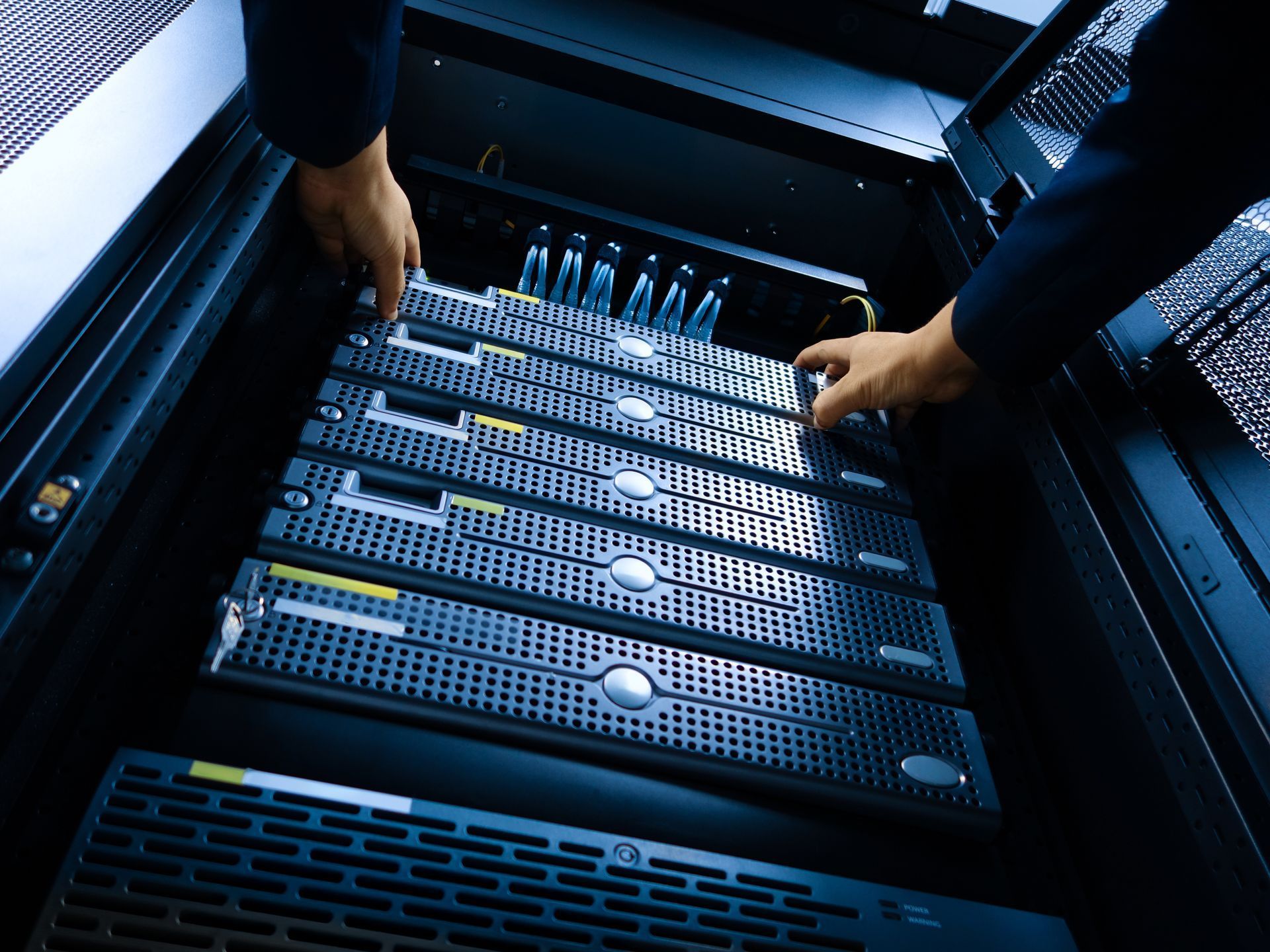 Hands adjusting servers inside a dark rack in a data center.