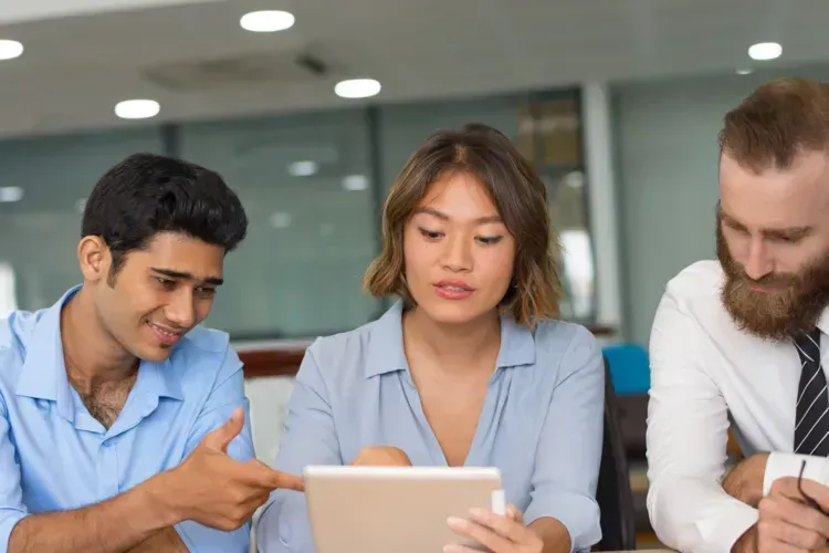Three coworkers looking at a tablet in an office. A man points to the screen.