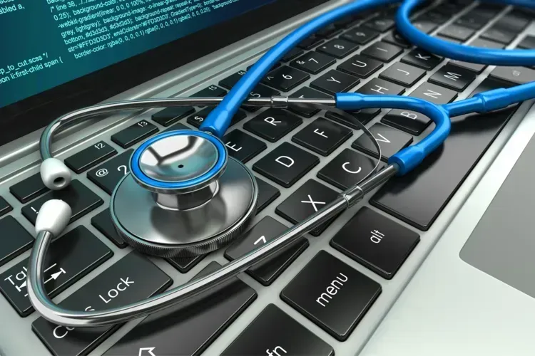 Blue stethoscope resting on a laptop keyboard; healthcare and technology concept.