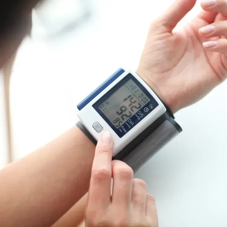 Person using a wrist blood pressure monitor, displaying a reading of 142/95.