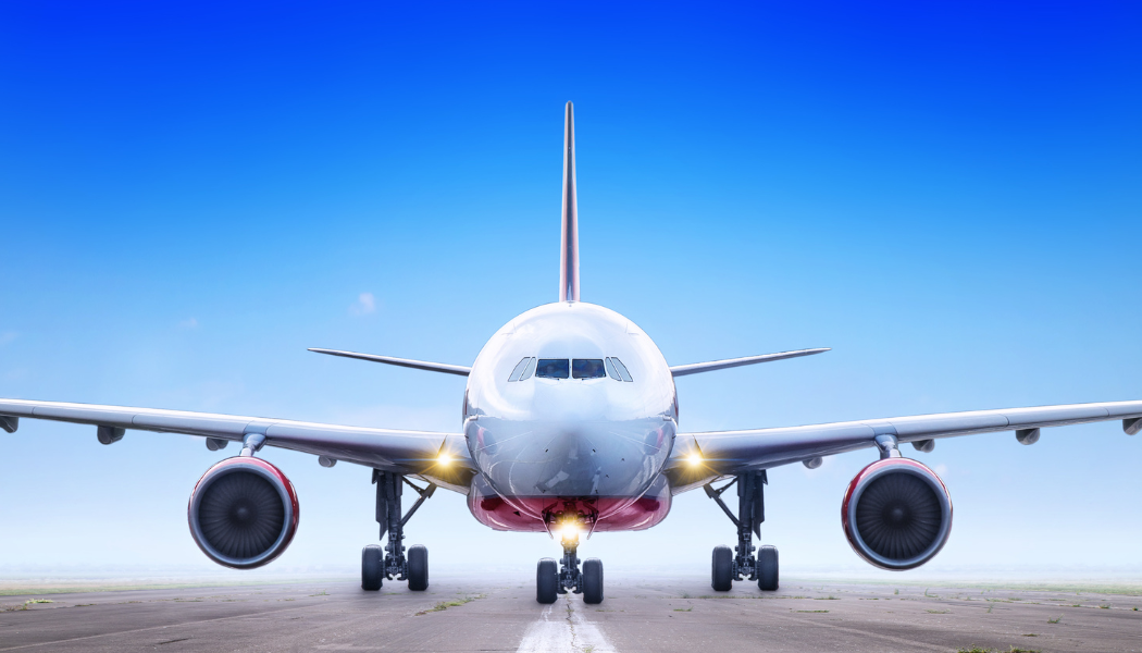 Airplane on a runway, facing the camera with wings spread, under a blue sky.
