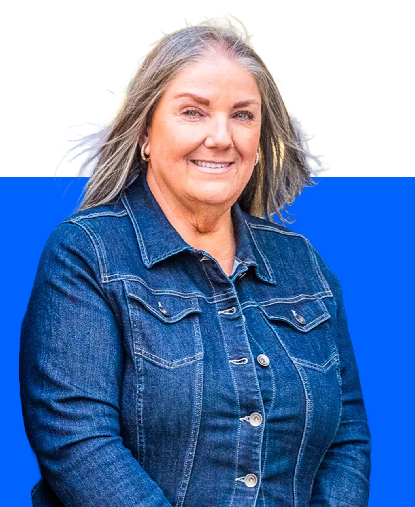 A person with shoulder-length gray hair wearing a dark denim jacket, smiling against a white and blue background.