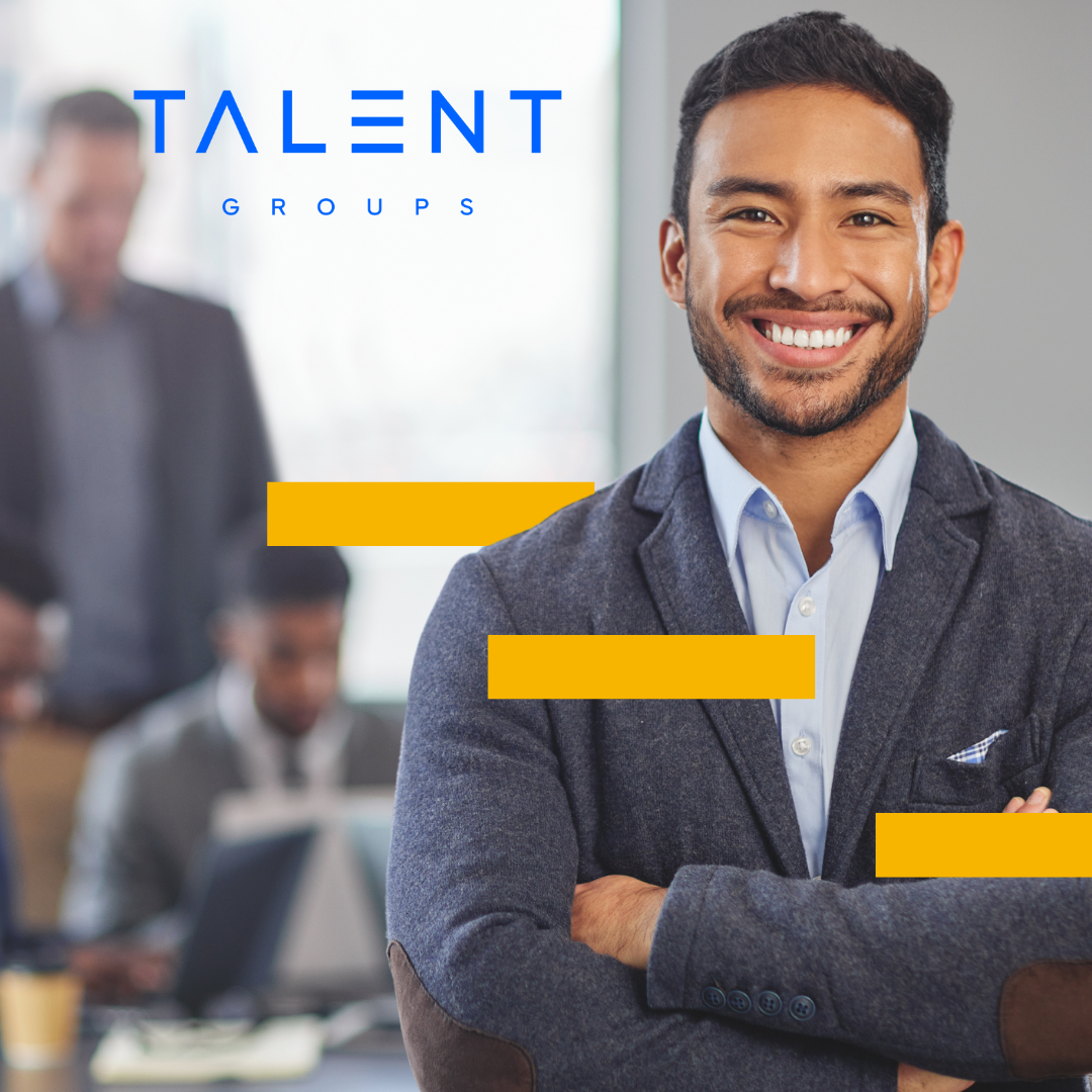 A smiling professional in a blazer with arms crossed in an office setting, with a 