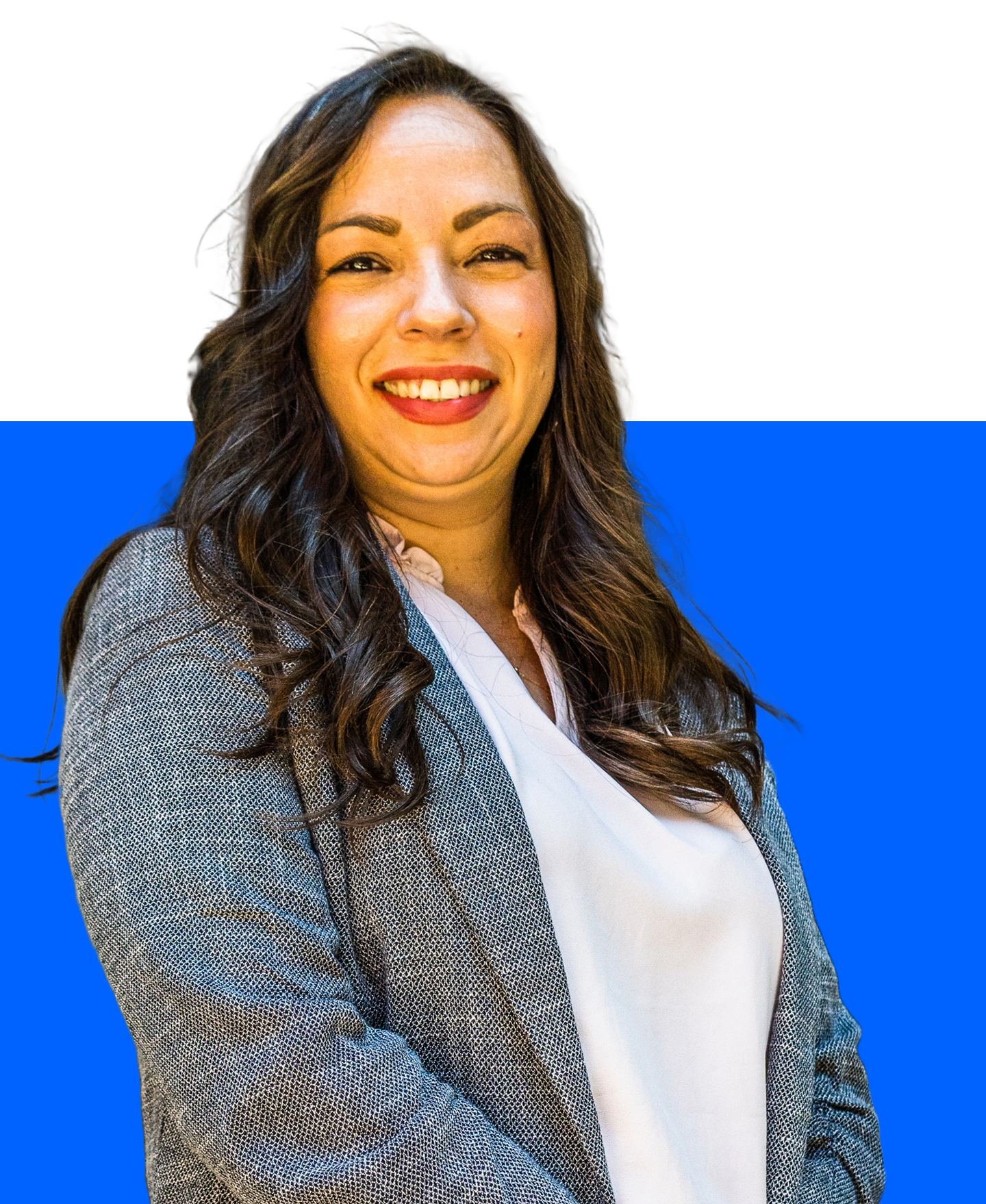 A person with long, wavy brown hair smiling, wearing a white shirt and a gray textured blazer against a blue background.