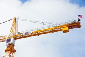 Yellow construction crane with American flag against a cloudy sky.