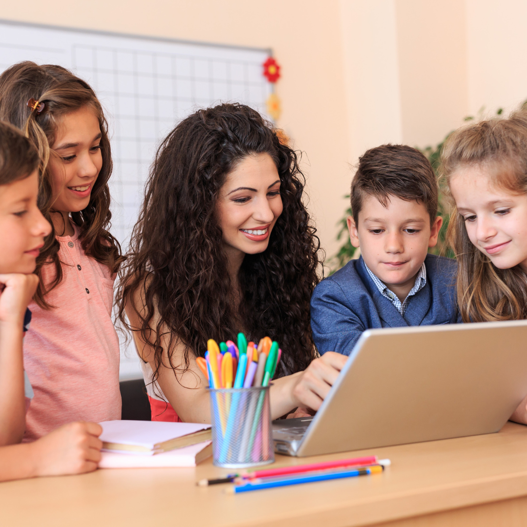 Teacher and students looking at laptop screen in classroom.