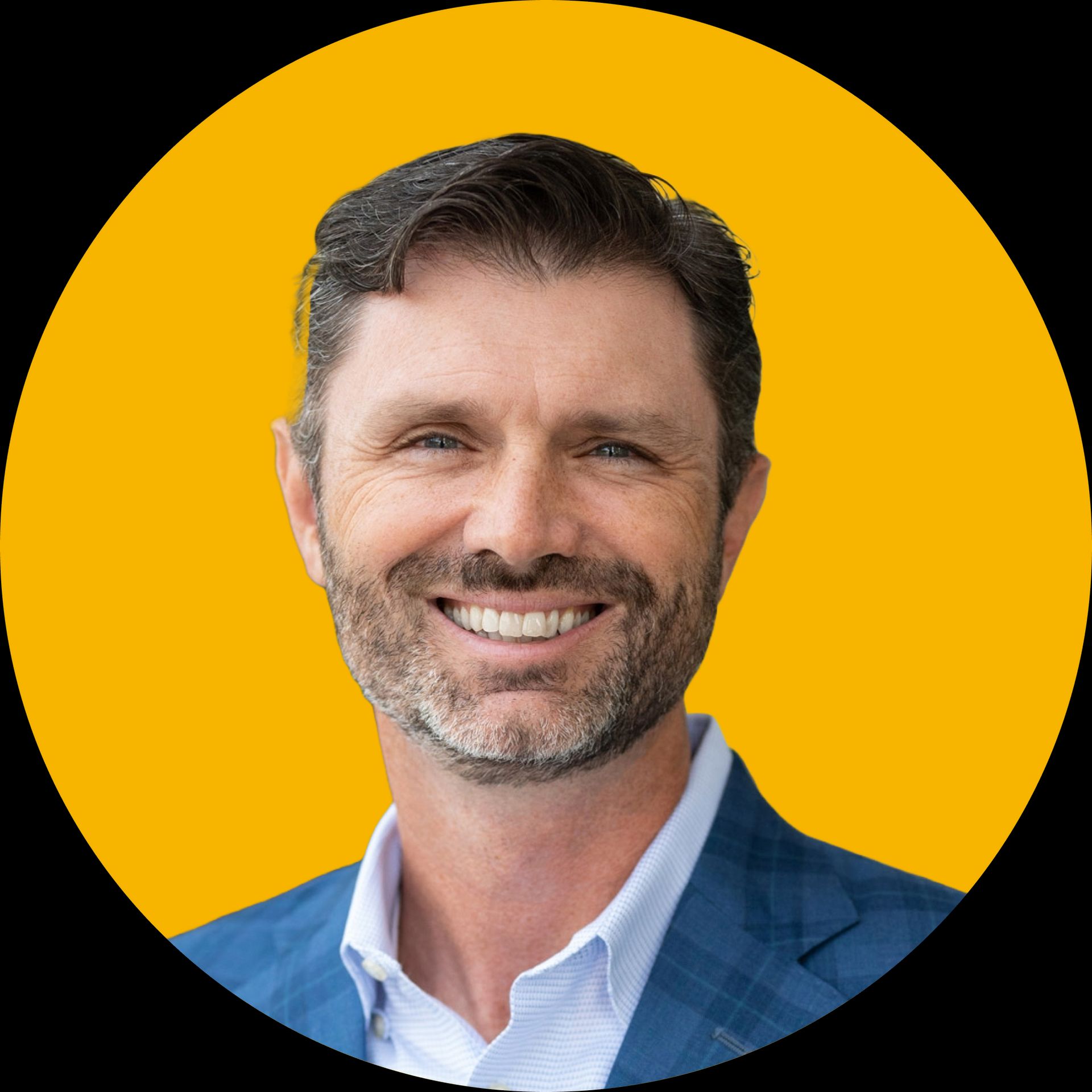 A smiling person with short dark hair and a beard, wearing a light blue dress shirt and a blue blazer against a yellow disc.