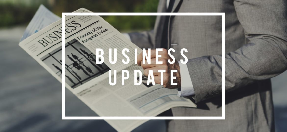 A person in a gray suit holds a business newspaper, with the text 